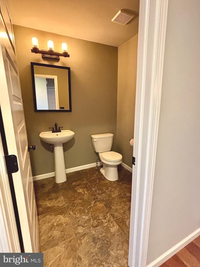 half bathroom with visible vents, toilet, a sink, and baseboards