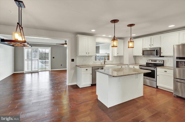 kitchen featuring stainless steel appliances, a kitchen island, white cabinets, light stone countertops, and decorative light fixtures