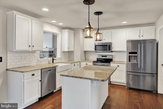 kitchen featuring stainless steel appliances, light stone counters, white cabinetry, and a center island