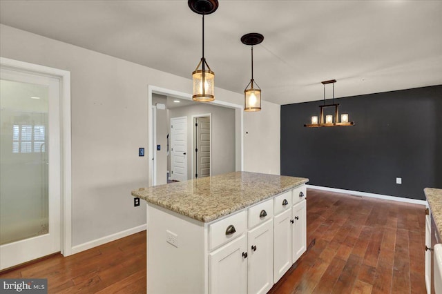 kitchen with light stone counters, dark wood-style flooring, white cabinets, a center island, and decorative light fixtures