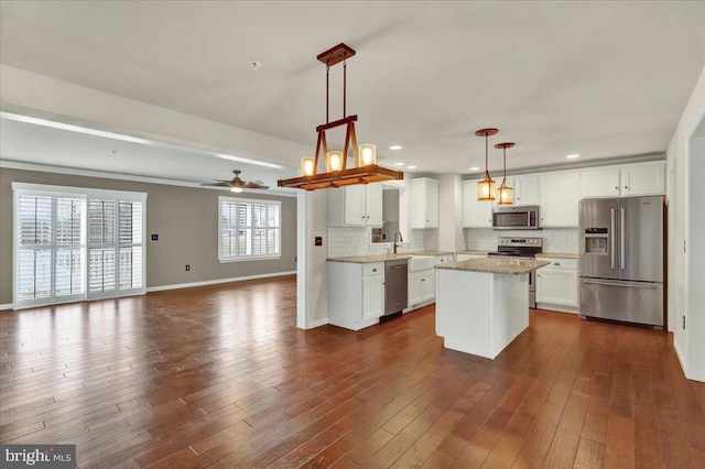 kitchen with white cabinetry, open floor plan, appliances with stainless steel finishes, a center island, and decorative light fixtures