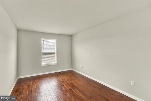 spare room featuring baseboards and dark wood-type flooring