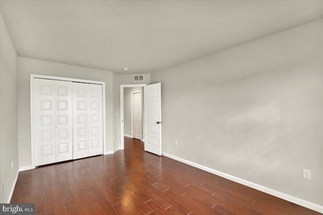 unfurnished bedroom with a closet, dark wood-style flooring, visible vents, and baseboards