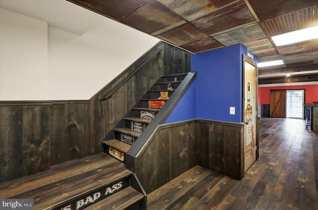 stairway featuring a wainscoted wall, wooden walls, and wood finished floors