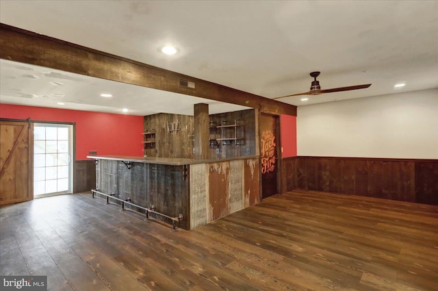 bar with a barn door, dark wood-type flooring, wainscoting, wood walls, and a bar