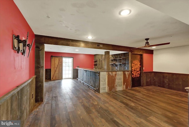 kitchen with dark wood-style flooring, a wainscoted wall, a barn door, ceiling fan, and wooden walls