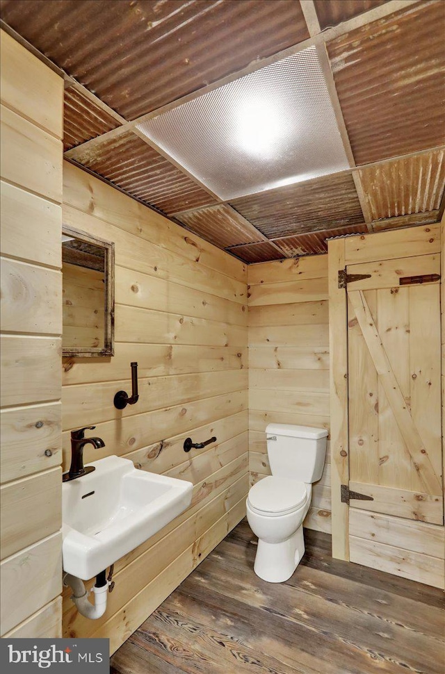 bathroom with a sink, wooden walls, toilet, and wood finished floors