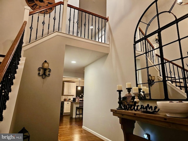 corridor featuring dark wood-style floors, baseboards, a high ceiling, and stairway