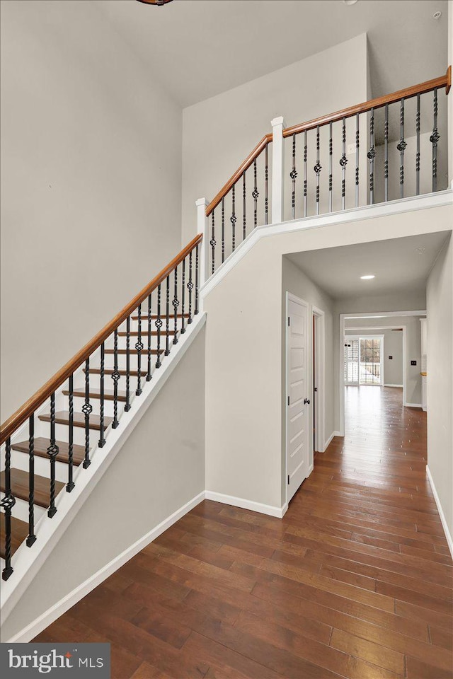 staircase with wood finished floors, a towering ceiling, and baseboards