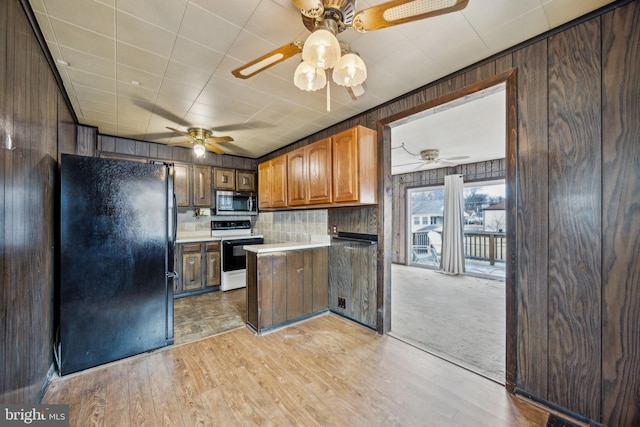 kitchen featuring range with electric cooktop, wooden walls, black refrigerator, ceiling fan, and light wood-type flooring