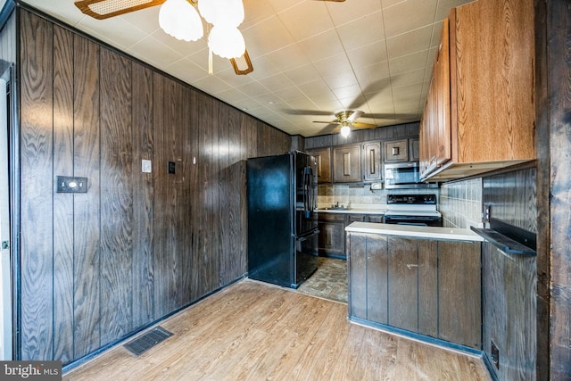 kitchen featuring black appliances, ceiling fan, light hardwood / wood-style floors, wood walls, and sink