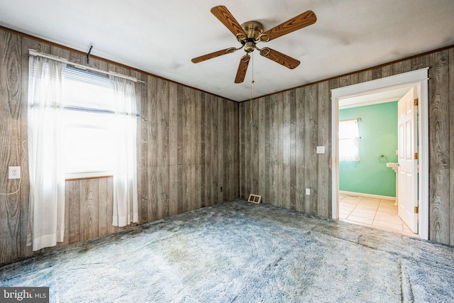 carpeted empty room with ceiling fan, crown molding, and wood walls