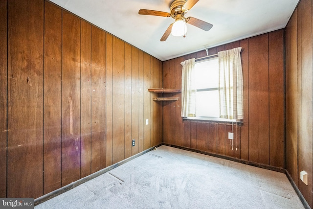 carpeted empty room with ceiling fan and wood walls