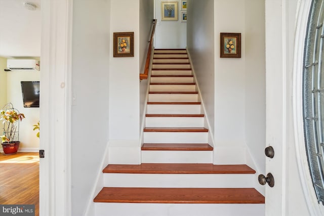 staircase with a wall mounted air conditioner and hardwood / wood-style flooring