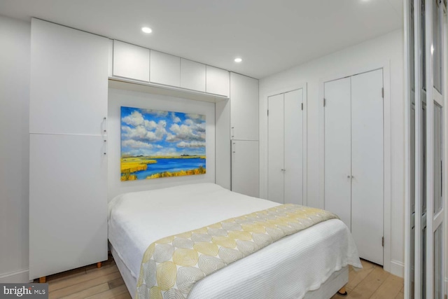 bedroom with light wood finished floors, multiple closets, and recessed lighting