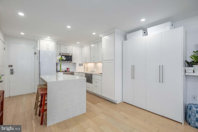 kitchen with light wood-style floors, light countertops, stainless steel microwave, and white cabinetry