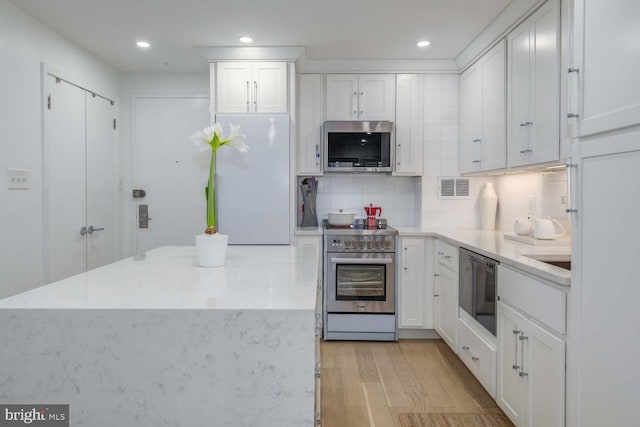 kitchen with light wood finished floors, appliances with stainless steel finishes, backsplash, and white cabinets