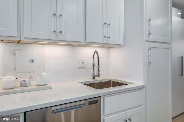 kitchen with light stone counters, decorative backsplash, stainless steel dishwasher, white cabinetry, and a sink