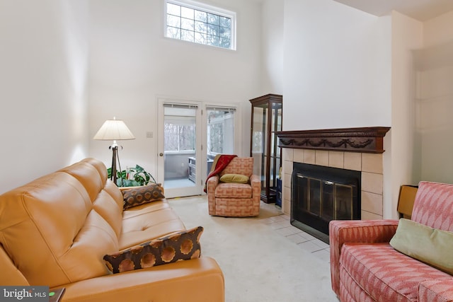 carpeted living area featuring a healthy amount of sunlight, a high ceiling, and a tile fireplace