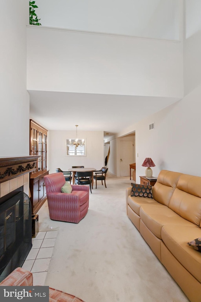 carpeted living area featuring a high ceiling, visible vents, a notable chandelier, and a tile fireplace