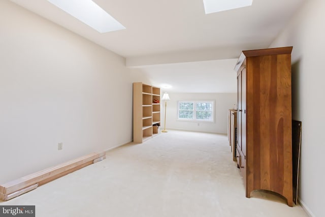 interior space featuring baseboards, a skylight, and light colored carpet