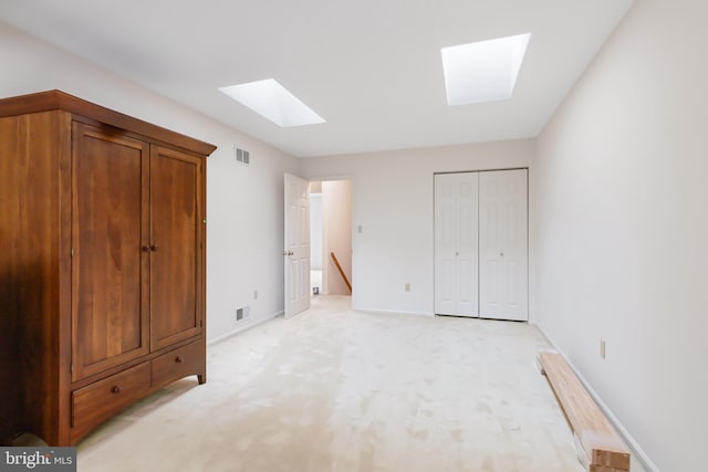 unfurnished bedroom with a skylight, a closet, visible vents, light carpet, and baseboards