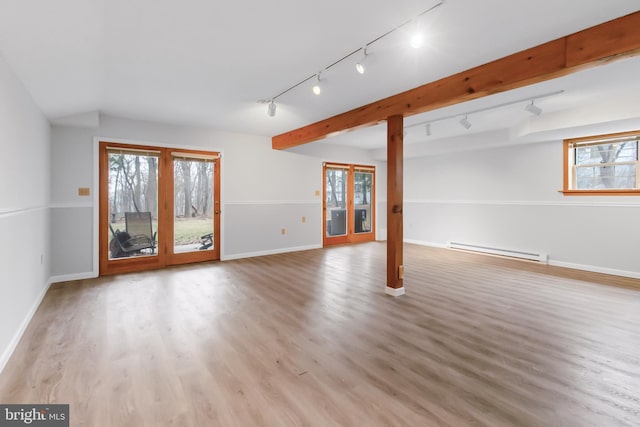 unfurnished living room featuring a healthy amount of sunlight, baseboard heating, and wood finished floors