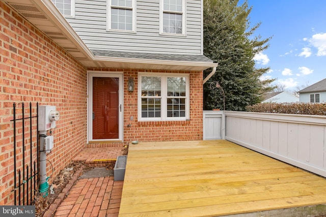 property entrance with a deck, a shingled roof, and brick siding