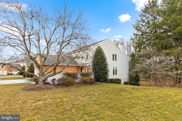 view of home's exterior with brick siding, a chimney, a lawn, a garage, and driveway