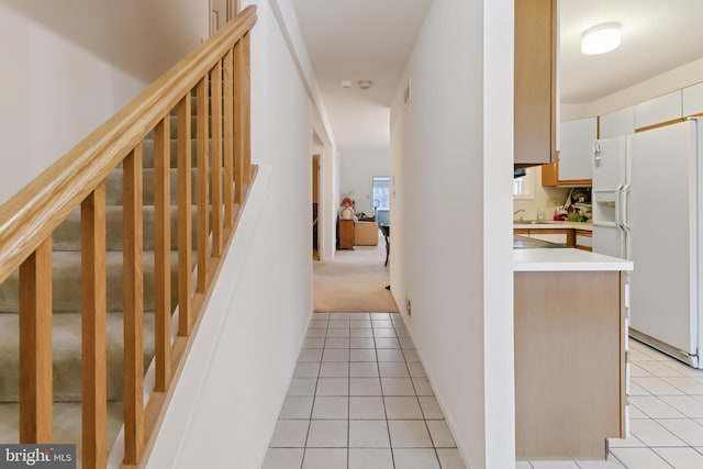 hall with light tile patterned floors, a sink, stairs, and light carpet