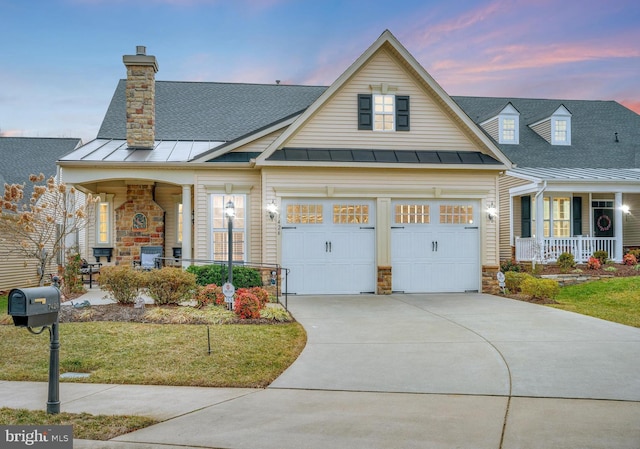 view of front of home featuring a lawn, a standing seam roof, a porch, stone siding, and concrete driveway