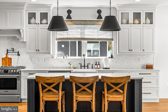 kitchen with stainless steel range with gas cooktop, hanging light fixtures, white cabinetry, and a breakfast bar area