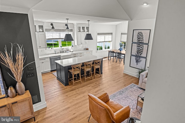 kitchen with decorative light fixtures, a kitchen island, stainless steel dishwasher, white cabinets, and a breakfast bar area