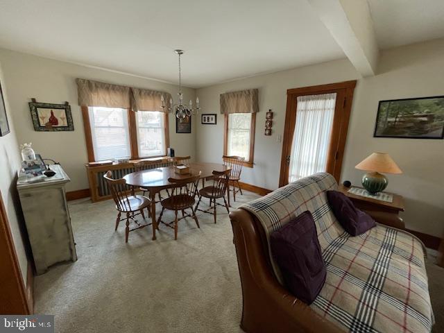 dining space featuring a notable chandelier, beamed ceiling, and light carpet