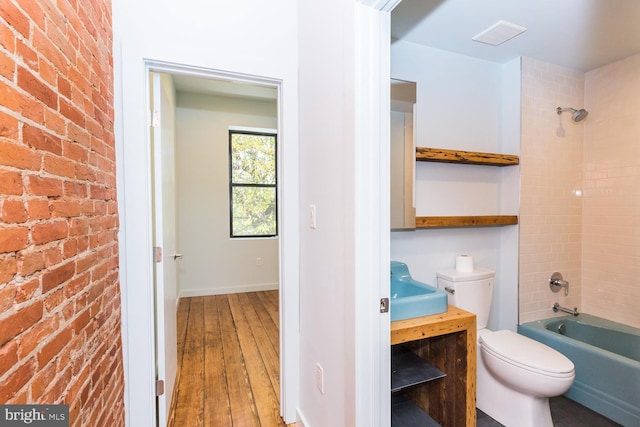 bathroom with brick wall, wood finished floors, bathtub / shower combination, and toilet