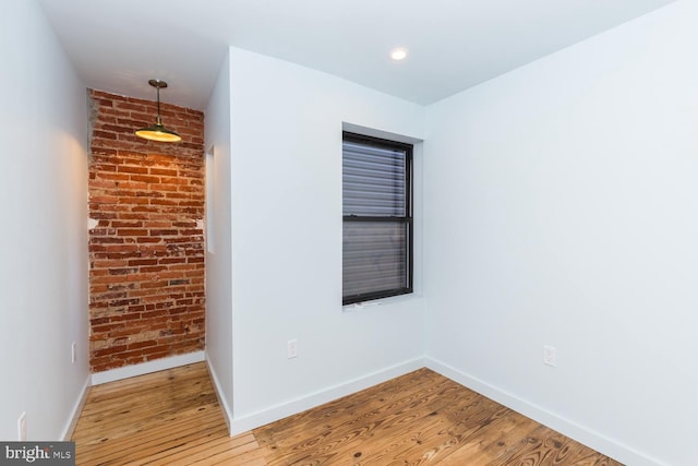 spare room with brick wall, wood finished floors, and baseboards