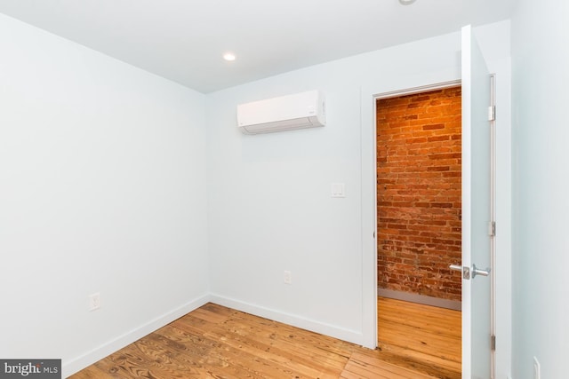 empty room with an AC wall unit, baseboards, brick wall, and wood finished floors