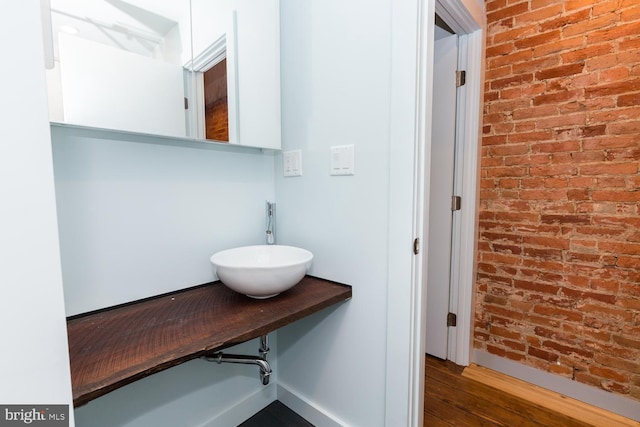 bathroom with a sink, brick wall, and wood finished floors