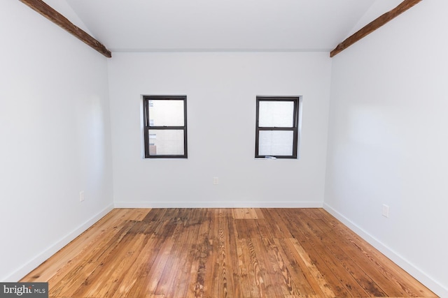 unfurnished room with a wealth of natural light, wood finished floors, beam ceiling, and baseboards