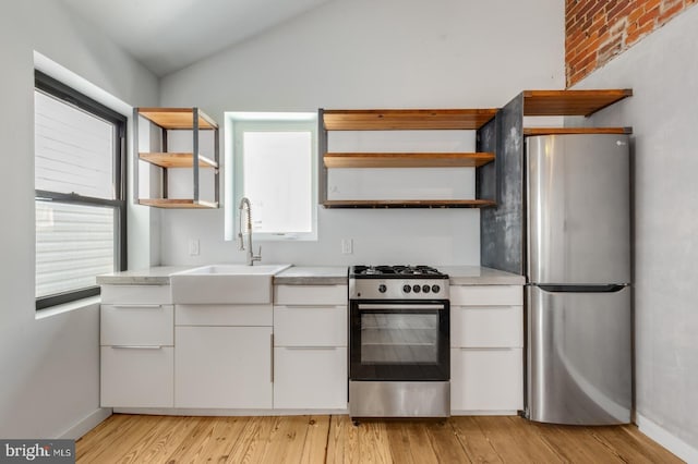 kitchen with stainless steel appliances, light countertops, white cabinets, a sink, and vaulted ceiling