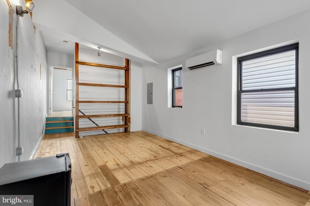 spare room with lofted ceiling, a wall unit AC, baseboards, electric panel, and light wood finished floors