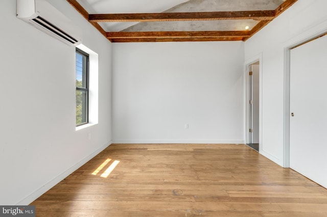 unfurnished room featuring baseboards, beamed ceiling, a wall unit AC, and light wood-style floors