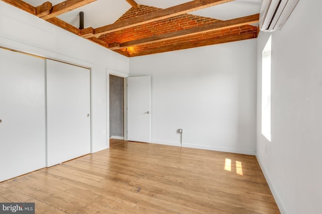 unfurnished bedroom with baseboards, brick ceiling, an AC wall unit, light wood-type flooring, and a closet