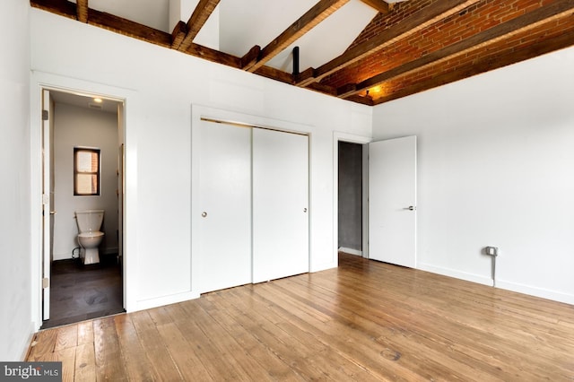 unfurnished bedroom with ensuite bath, light wood-style flooring, a closet, and beamed ceiling