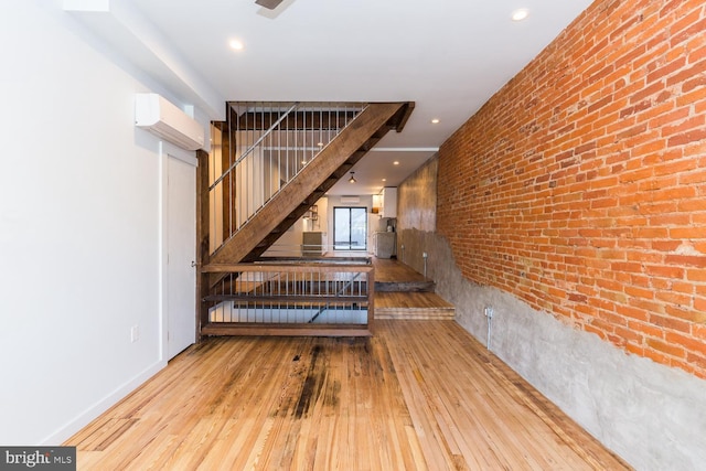 interior space with a wall unit AC, recessed lighting, brick wall, wood finished floors, and baseboards