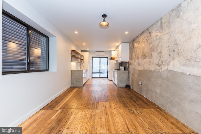 unfurnished living room featuring light wood-style floors, a wall mounted AC, baseboards, and recessed lighting