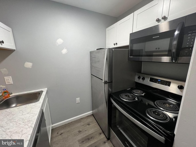 kitchen with light hardwood / wood-style floors, appliances with stainless steel finishes, white cabinetry, and sink