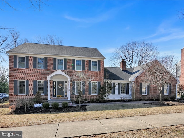 colonial inspired home with brick siding, a chimney, and a front yard