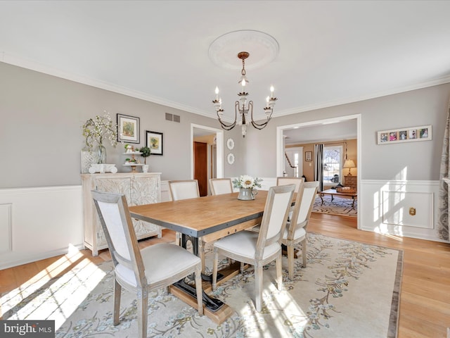 dining room featuring a chandelier, visible vents, light wood-style floors, wainscoting, and crown molding