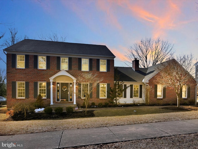 colonial-style house featuring brick siding and a chimney